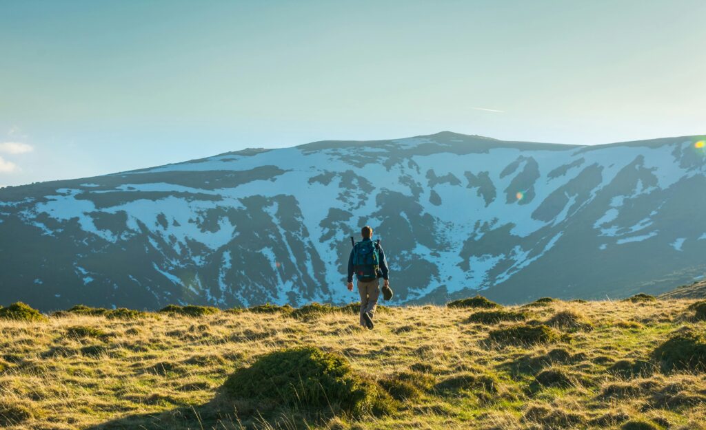 Five Lessons the Mountains Teach You About Life An adventurer walks through a sunlit grassland toward a snow-capped mountain, embodying freedom and exploration.